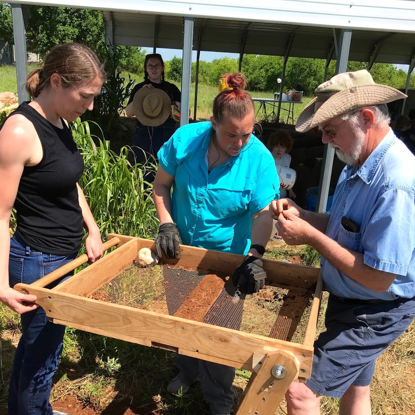 Excavators look over artifacts found while screening dirt.