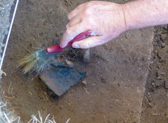 A person uses a paintbrush to clean off a piece of pottery.